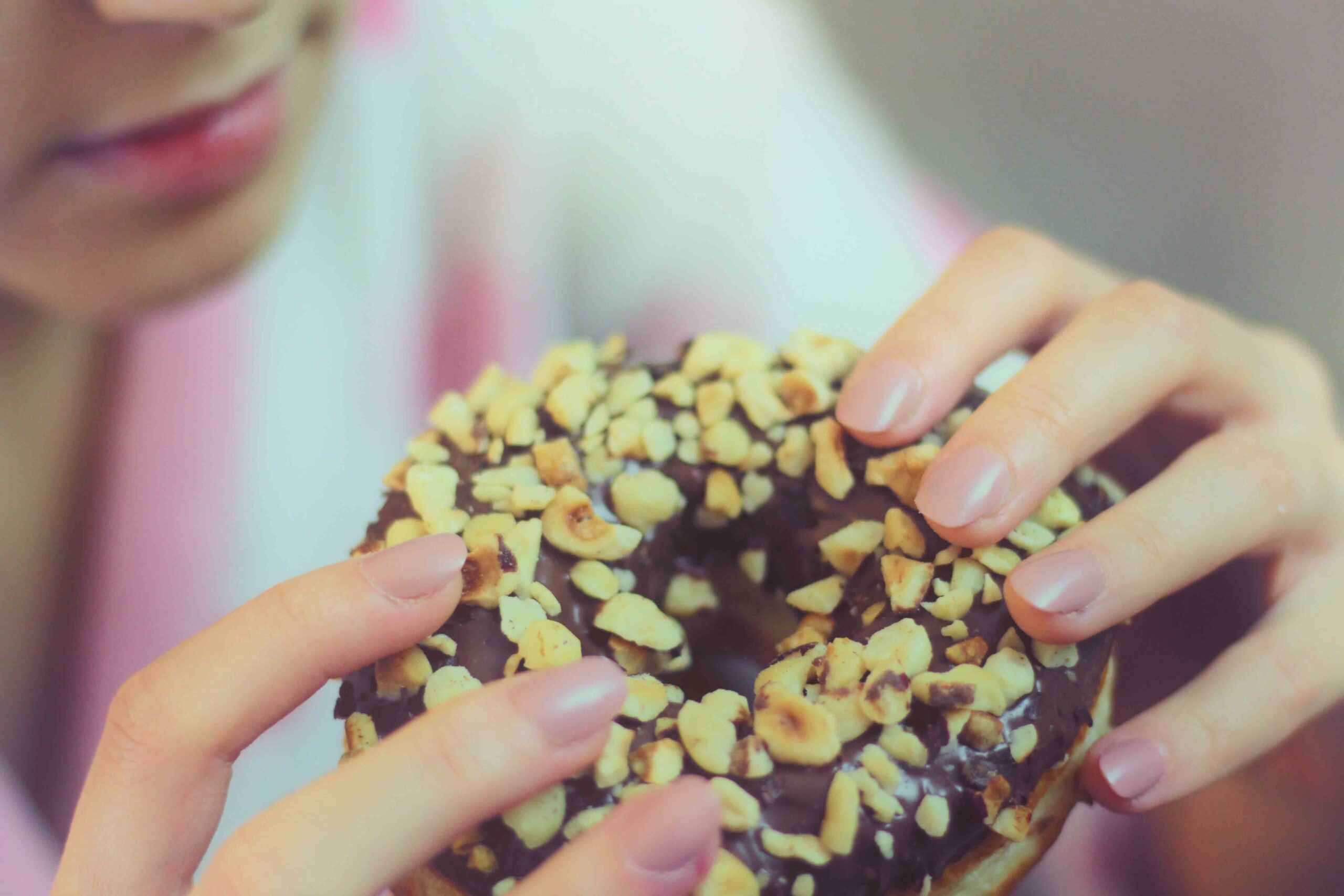 Pessoa comendo rosquinha tipo donuts de chocolate